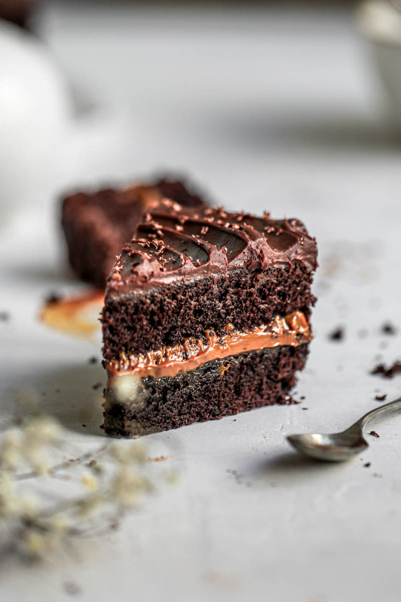 45° shot of one slice of chocolate dulce de leche cake with a spoon out of focus on the right hand side