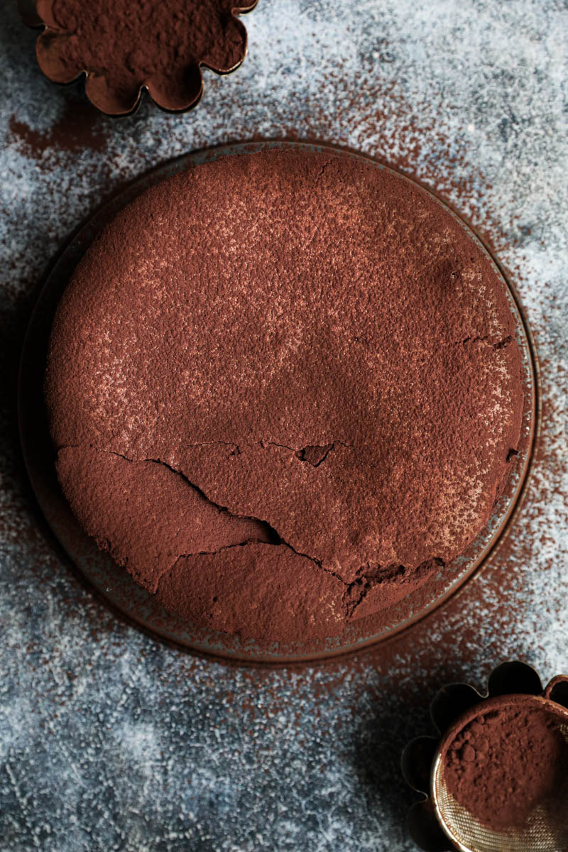 Whole chocolate fudge cake seen from above sprinkled with cocoa powder.