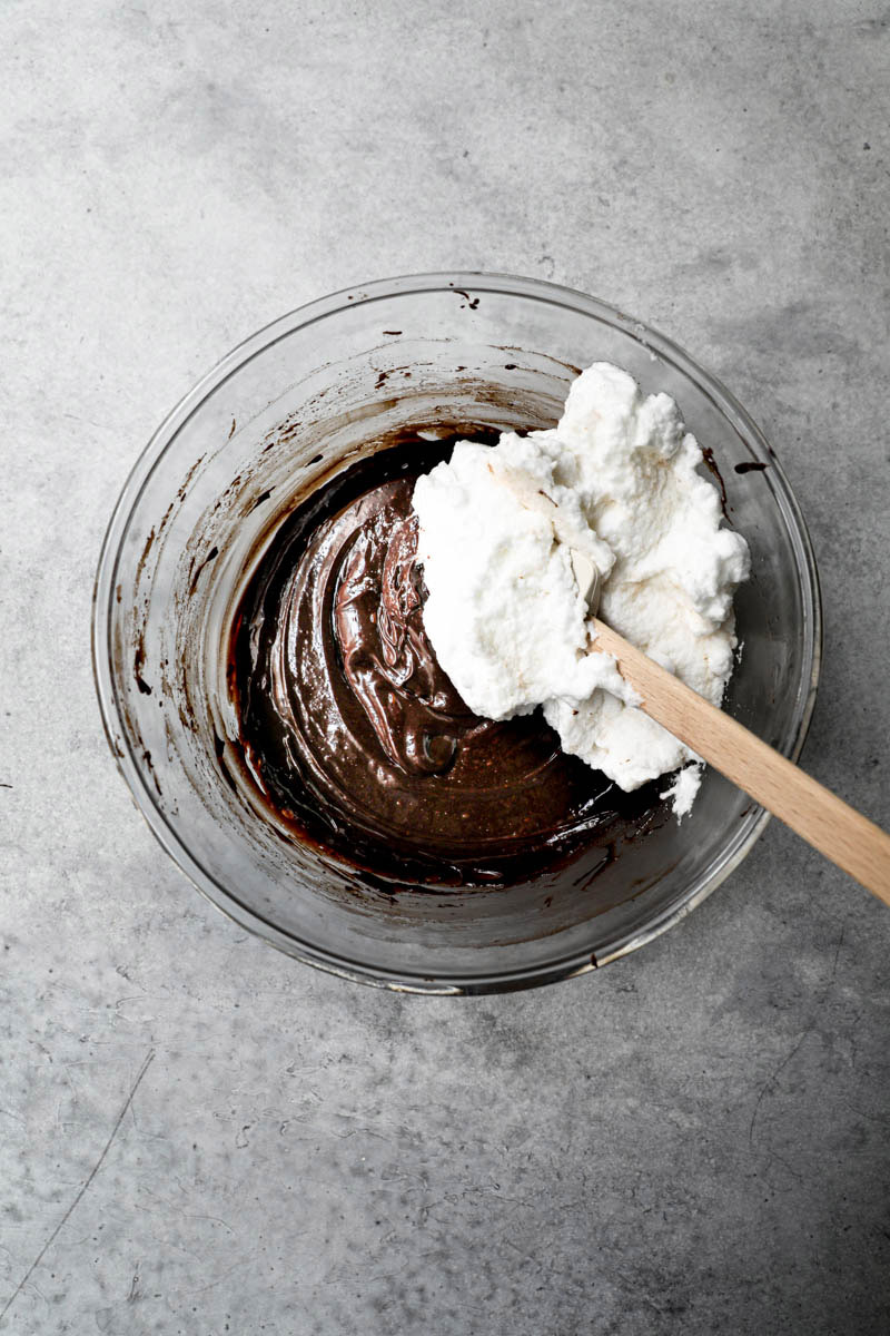 A portion of the egg whites inside of the chocolate mixture in a glass bowl.