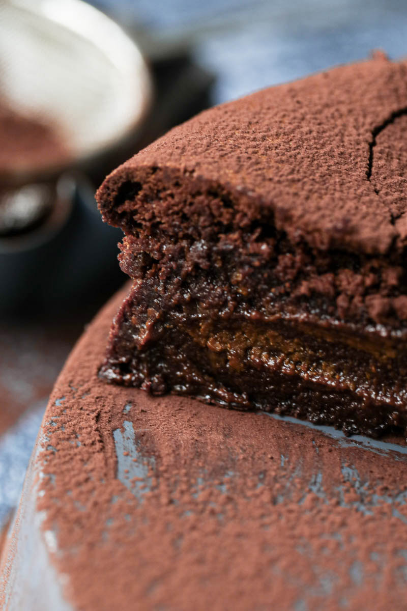 Closeup of a slice of chocolate fudge on a grey tray with cocoa powder around.