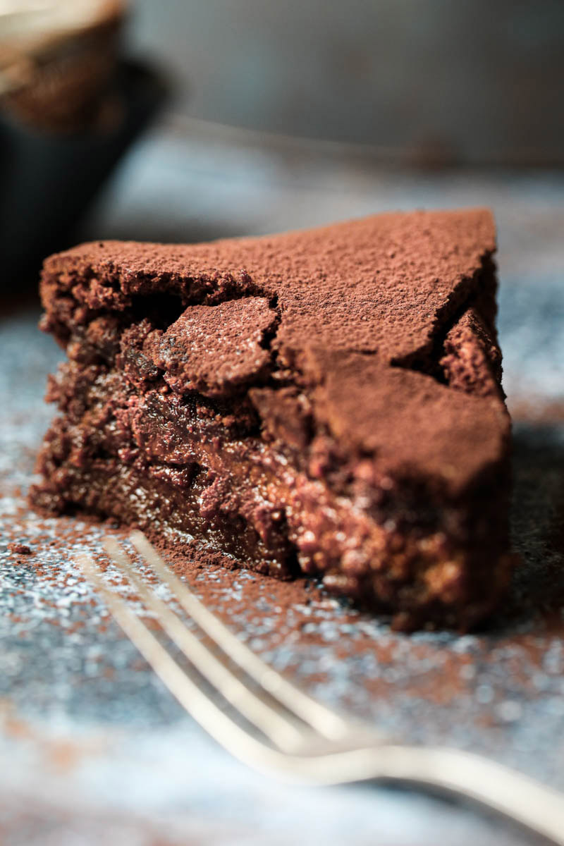 One slice of chocolate fudge cake seen from the side with a fork on the bottom corner.