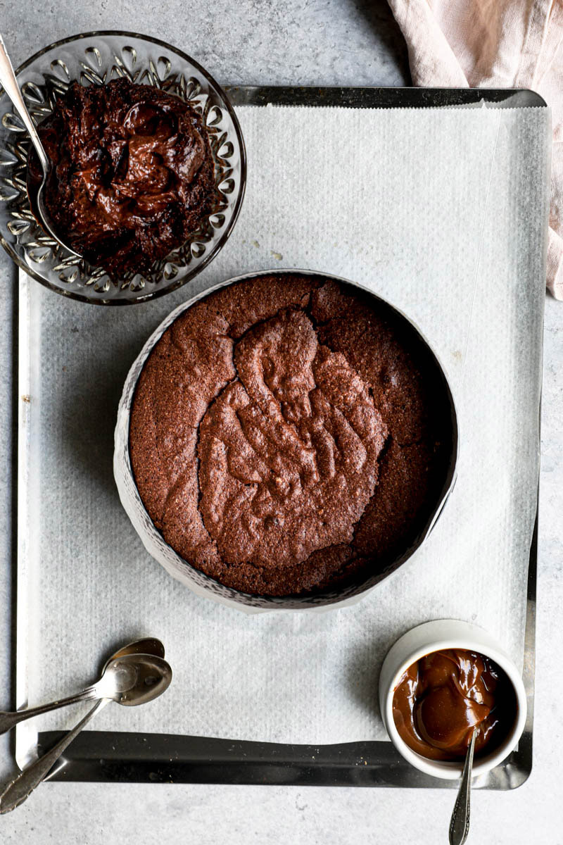 2/3 of the baked chocolate fudge cake on a baking tray with the remaining third in a glass bowl and dulce de leche in a small white container.