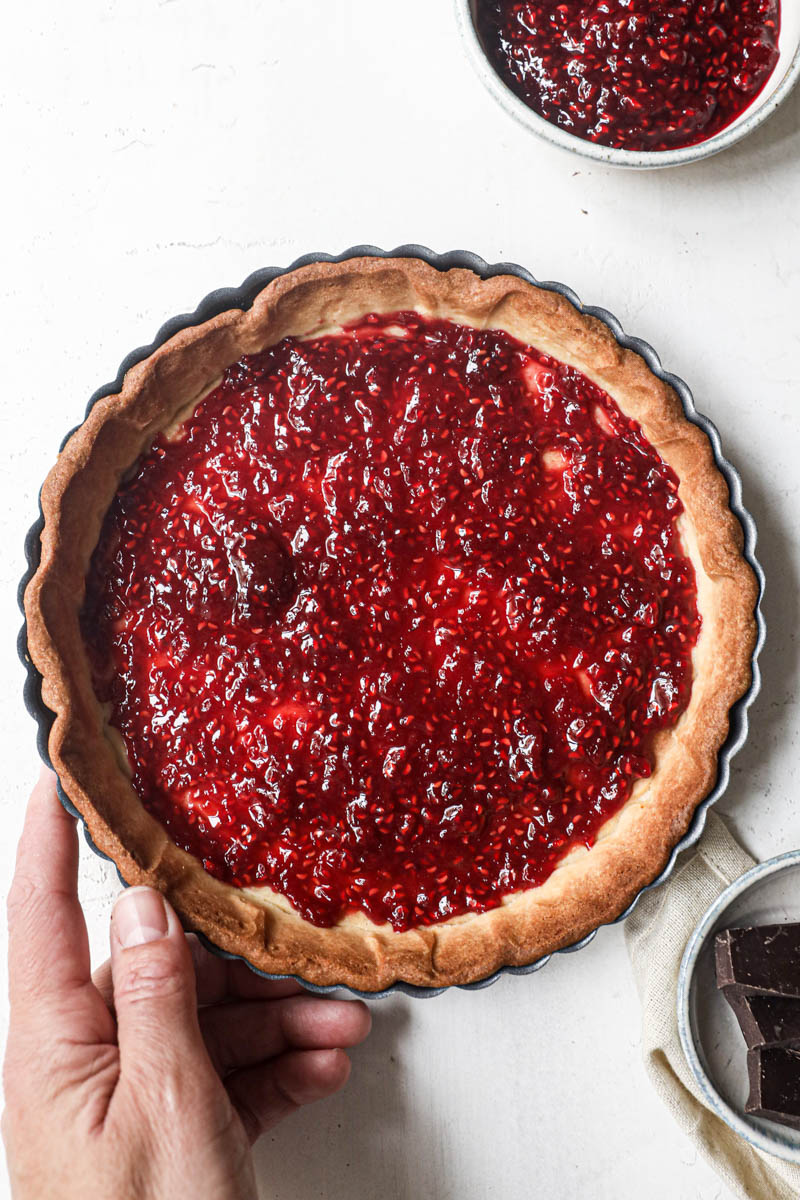 A hand holding the the shortbread crust filled with raspberry jam.