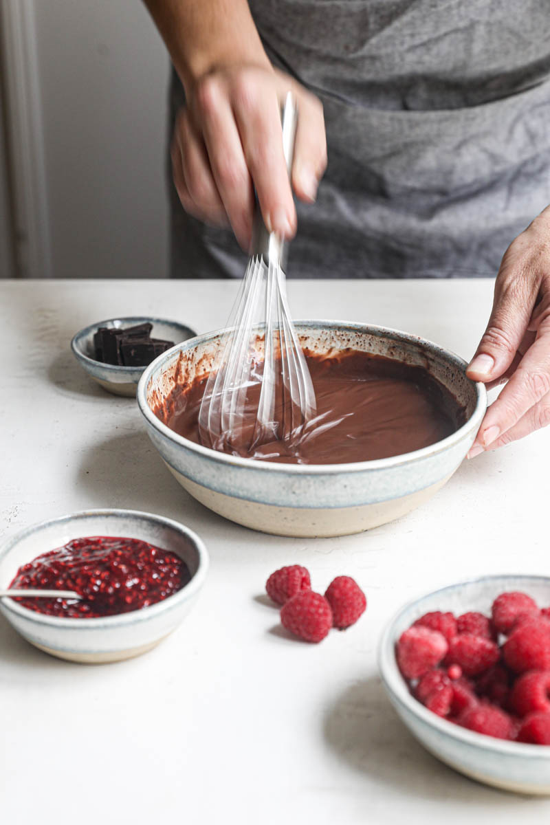 2 hand whisking the chocolate ganache inside a bowl.