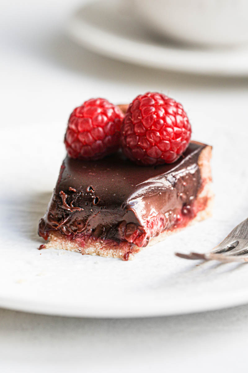 Once slice of chocolate ganache raspberry tart on a white plate with a fork on the side.