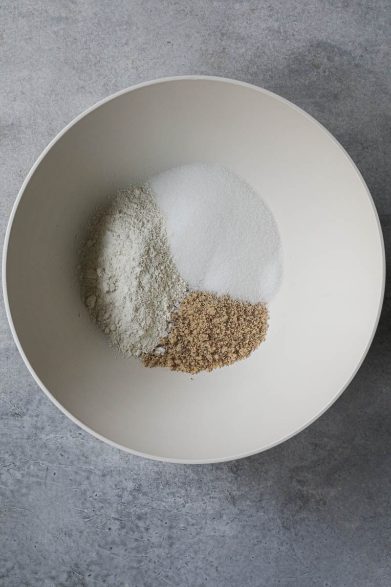 A beige bowl with the sugar, hazelnut meal and the flour inside a beige bowl.