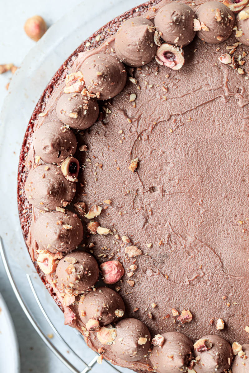 A closeup of half the chocolate hazelnut cake topped with whipped milk chocolate ganache on top of a wire rack.