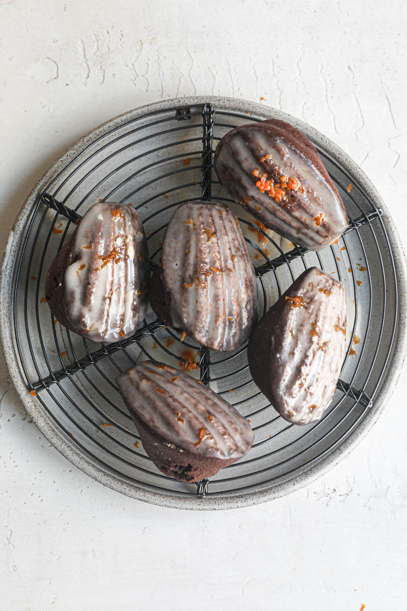 The orange glazed chocolate madeleines resting on top of a wire rack.