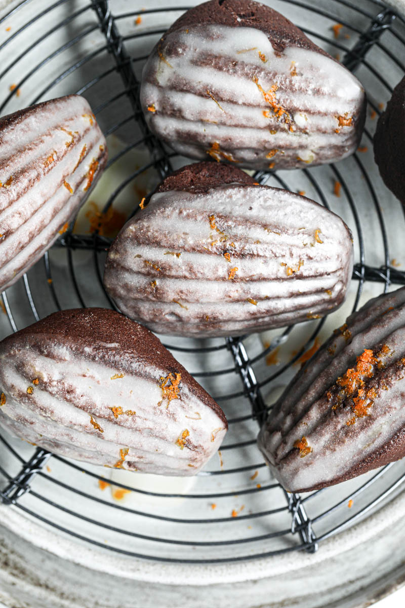 Closeup of the orange glazed chocolate madeleines resting on top of a wire rack after the glaze has set.