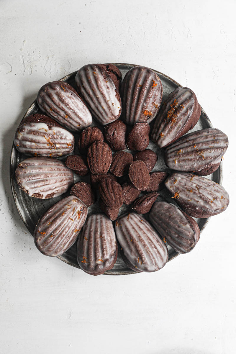 The orange glazed chocolate madeleines disposed in a circular manner on a grey plate.