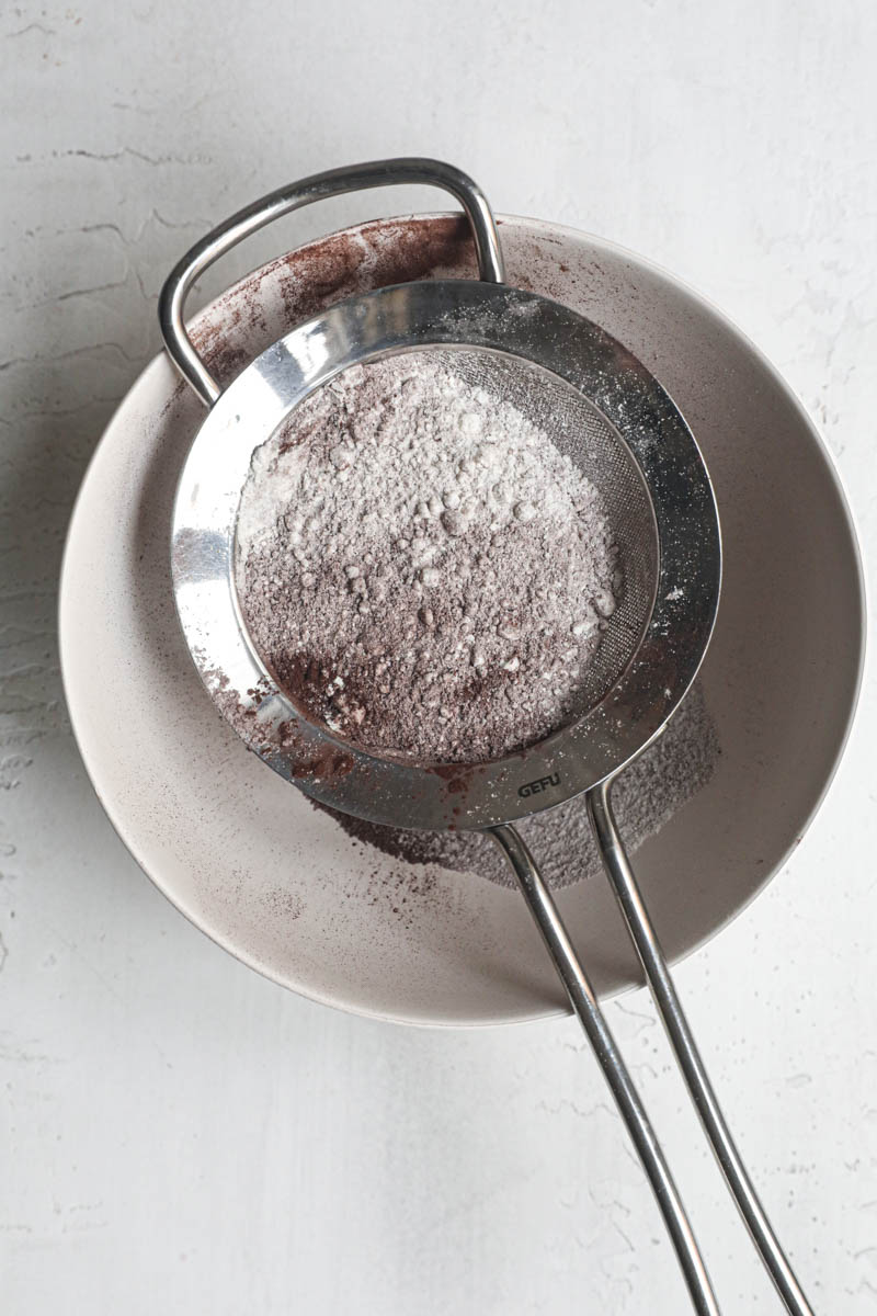 THe flour and cocoa powder inside a sift on top of a white bowl.