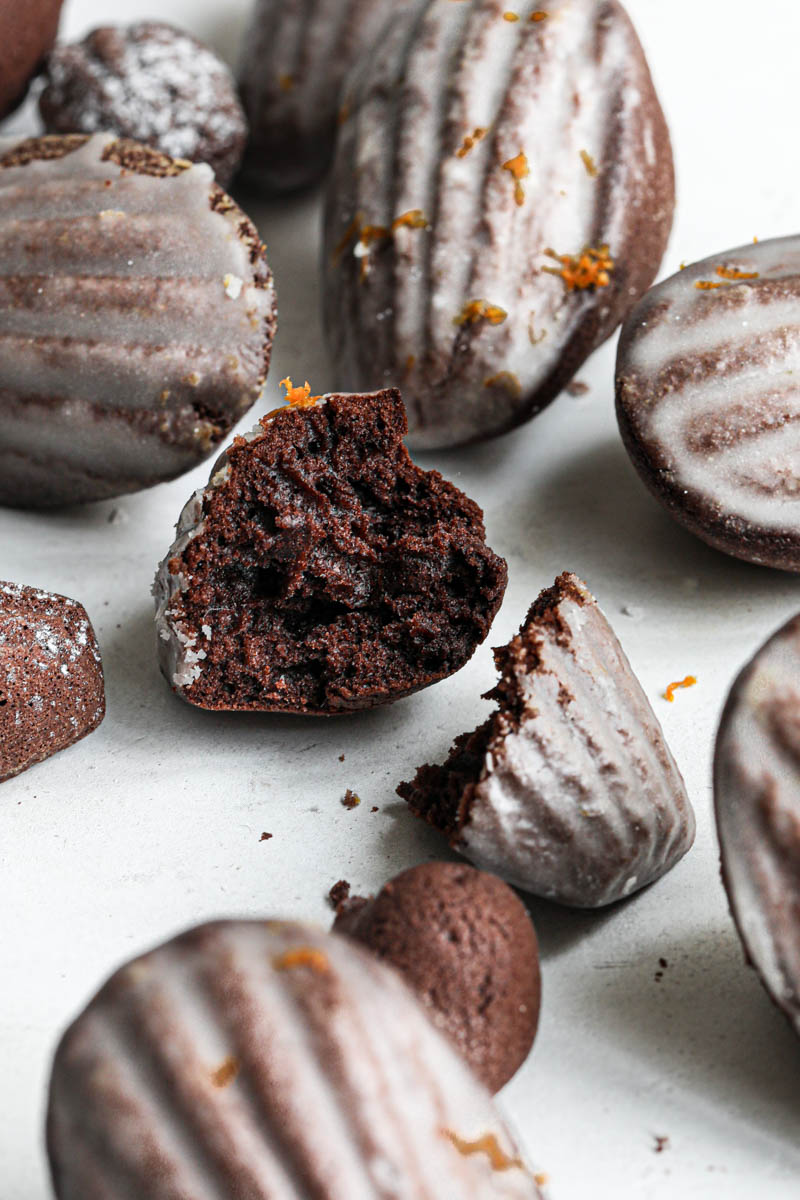 One orange glazed chocolate madeleine sliced open with other madeleines around it.