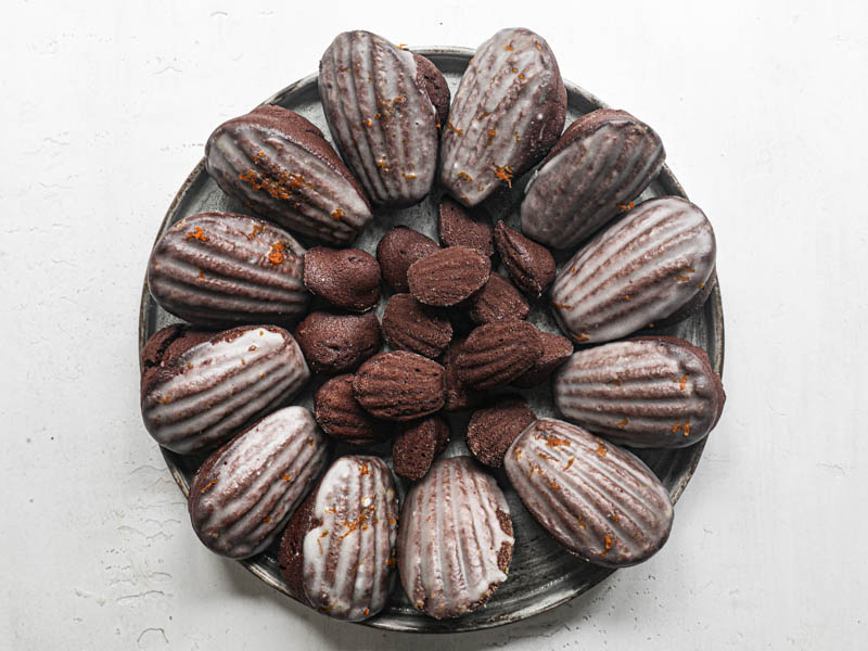 The orange glazed chocolate madeleines disposed in a circular manner on a grey plate.