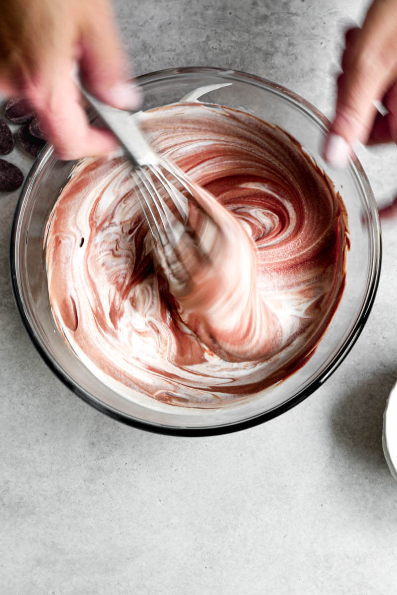 Overhead shot of 2 hands folding in the whipped cream into the chocolate ganache