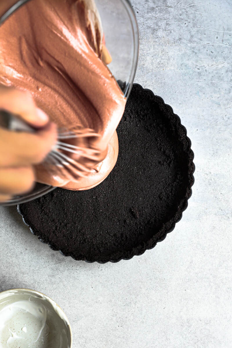 2 hand pouring the chocolate mousse over the oreo pie crust