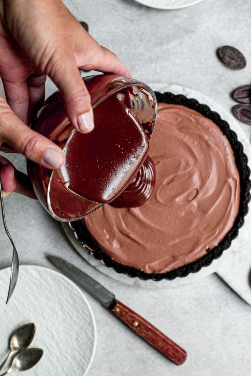 Overhead shot of 2 hands pouring the chocolate ganache over the tart