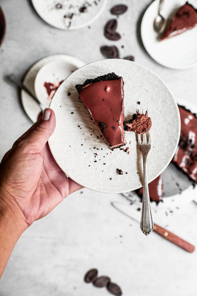 Overhead shot of one hand holding a white plate with a slice of chocolate mousse pie
