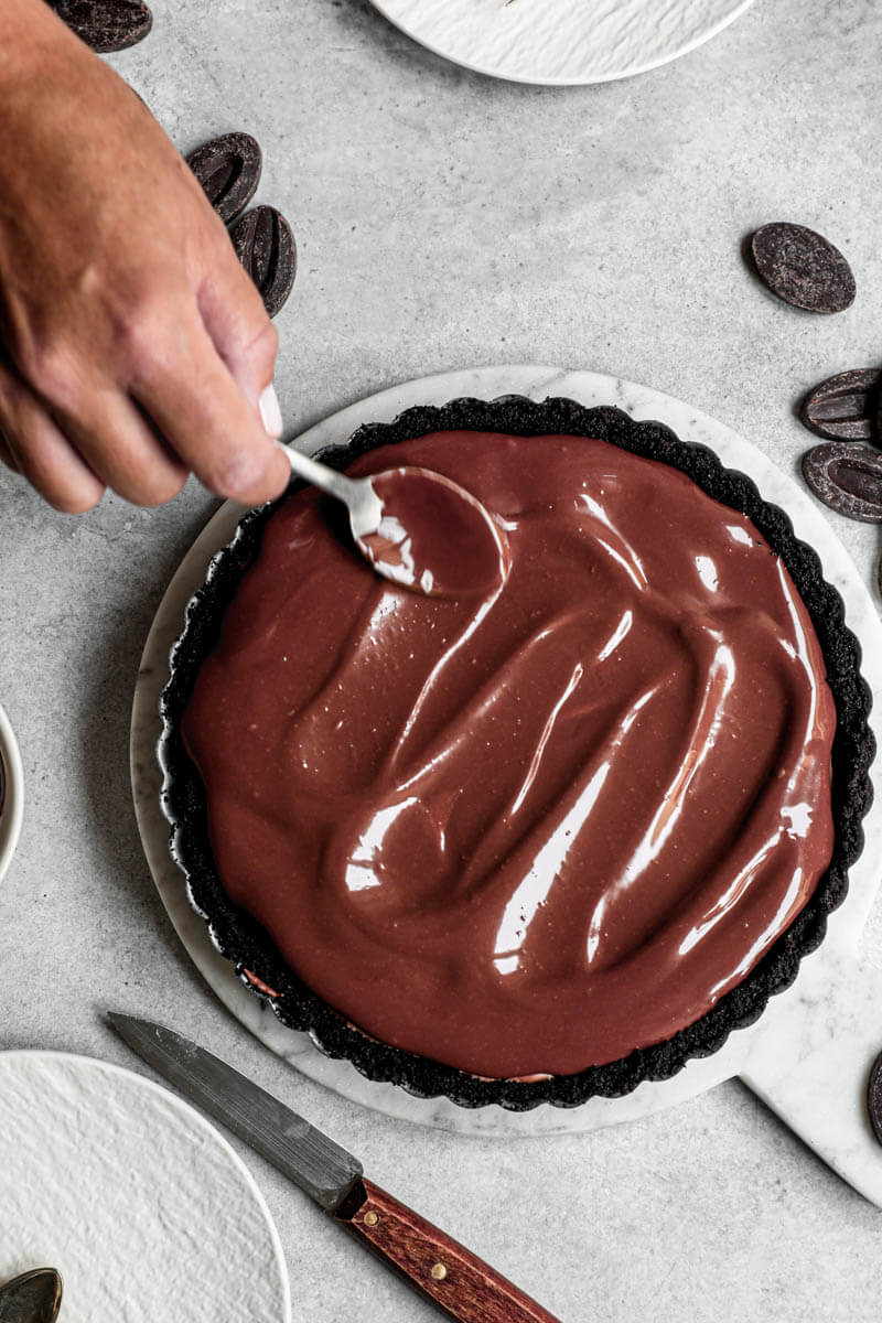 Overhead shot of one hand spreading the chocolate ganache using a spoon