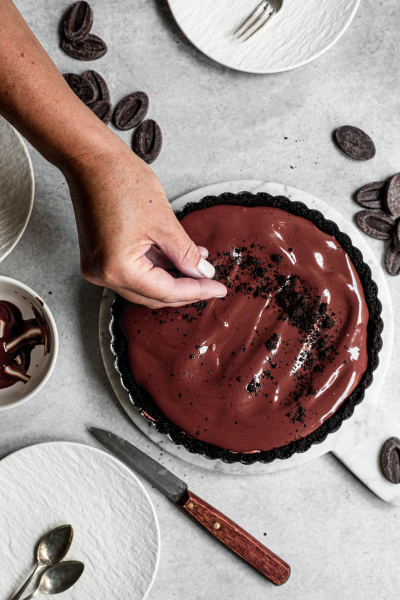 Overhead shot of one hand sprinkling crushed oreos over the chocolate mousse pie