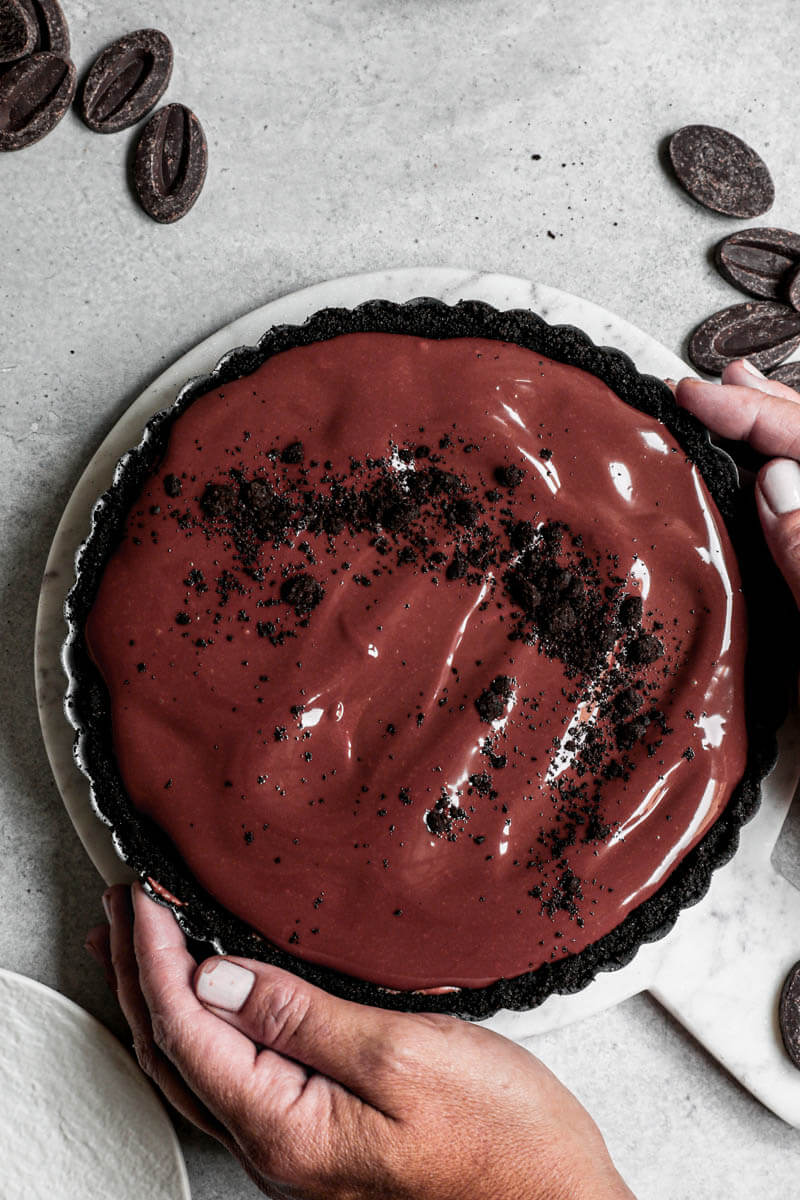 Overhead closeup shot of 2 hands holding the chocolate mousse pie in the pie tin