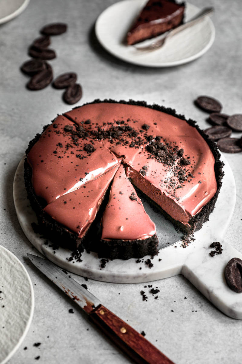 45° shot of the sliced chocolate mousse cake on a marble serving platter with a slice on a plate at the back