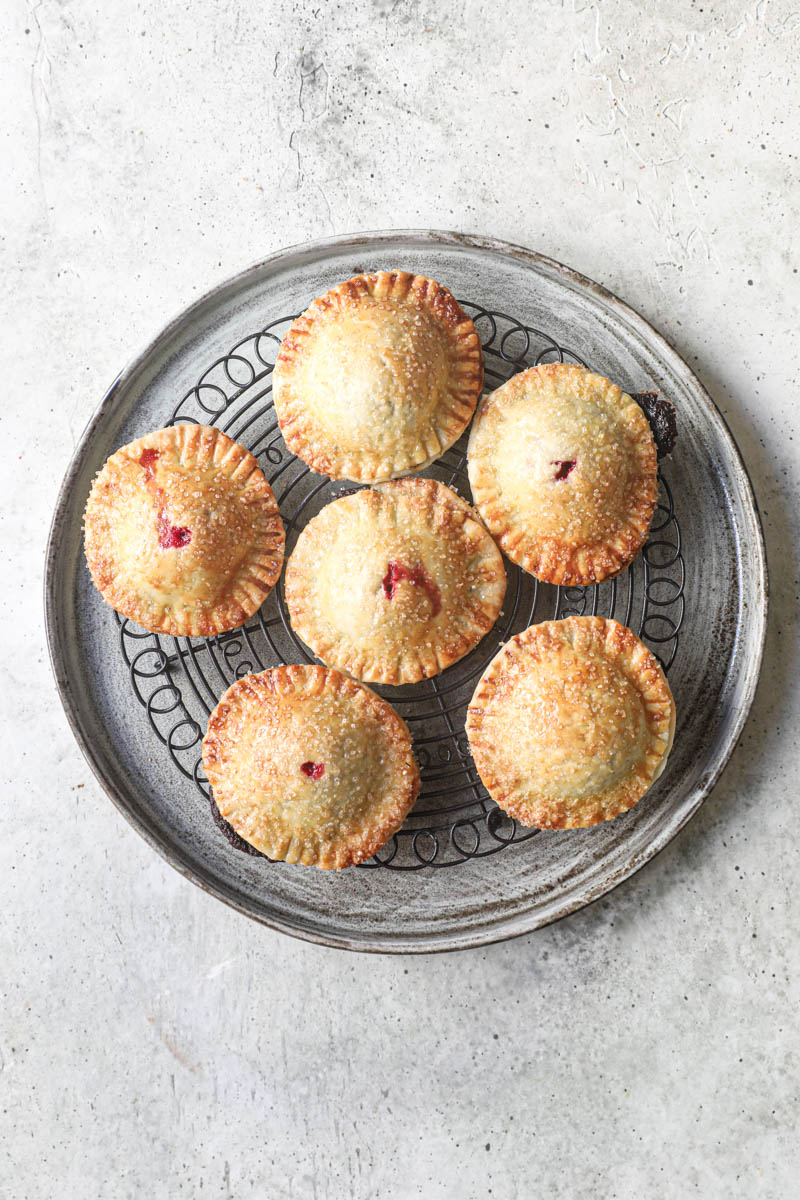 5 baked mini hand pies placed over a wire rack and on a grey plate..