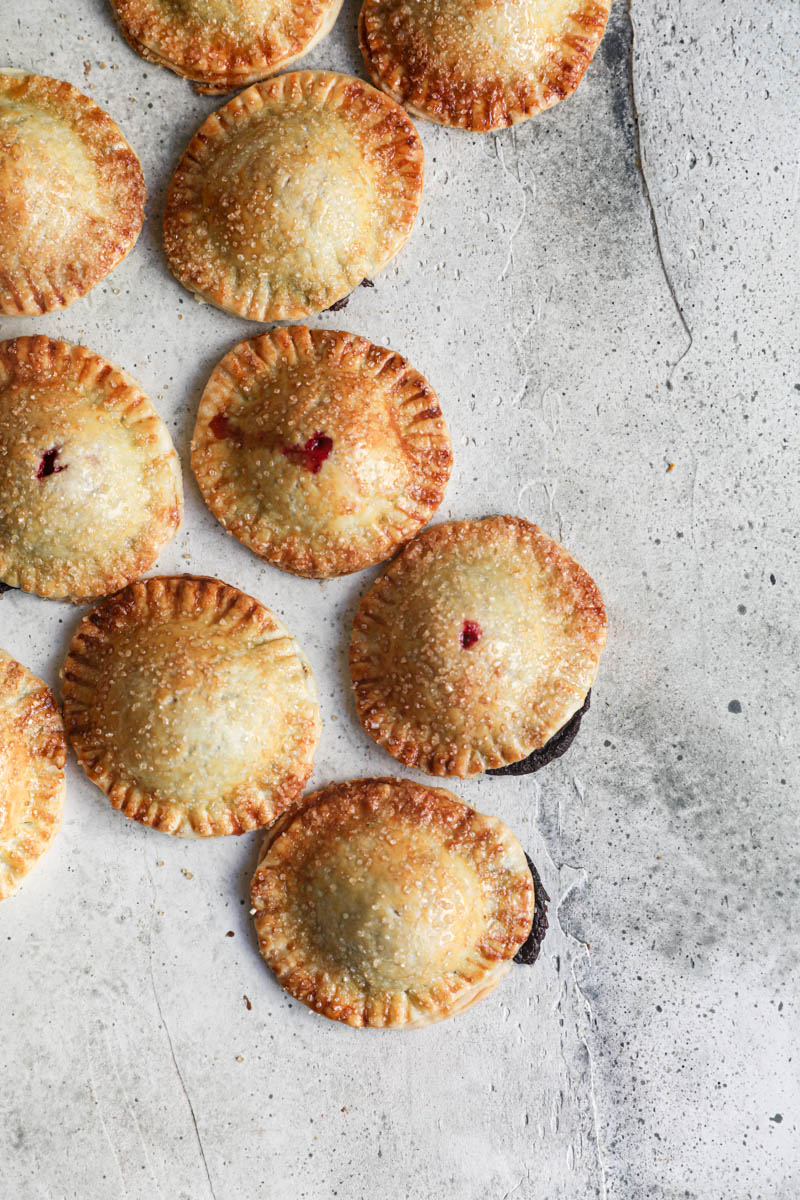 The chocolate raspberry hand pies disposed over a green surface in an irregular maner.