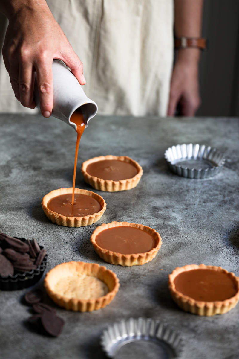 90° shot of a hand pouring salted caramel onto the tart shells