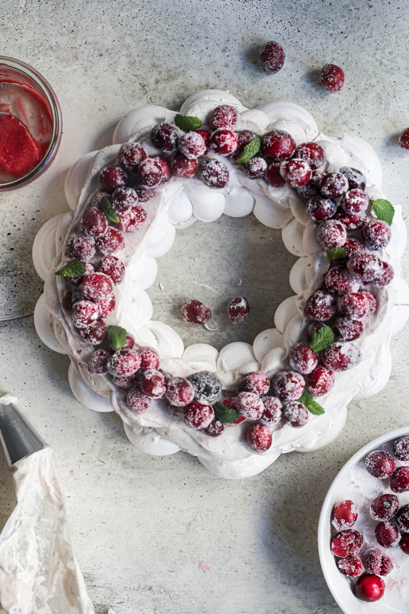 The Swiss meringue pavlova wreath covered with the cranberry cream and topped with sugar cranberries and some small mint leaves.