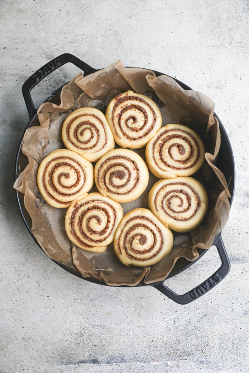 The cinnamon rolls ready for the oven inside a black cast iron pan lined with parchment paper.
