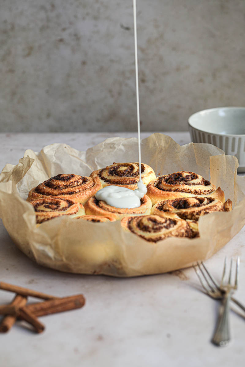 The milk glazed pouring over the baked brioche cinnamon rolls with a spoon on the side.