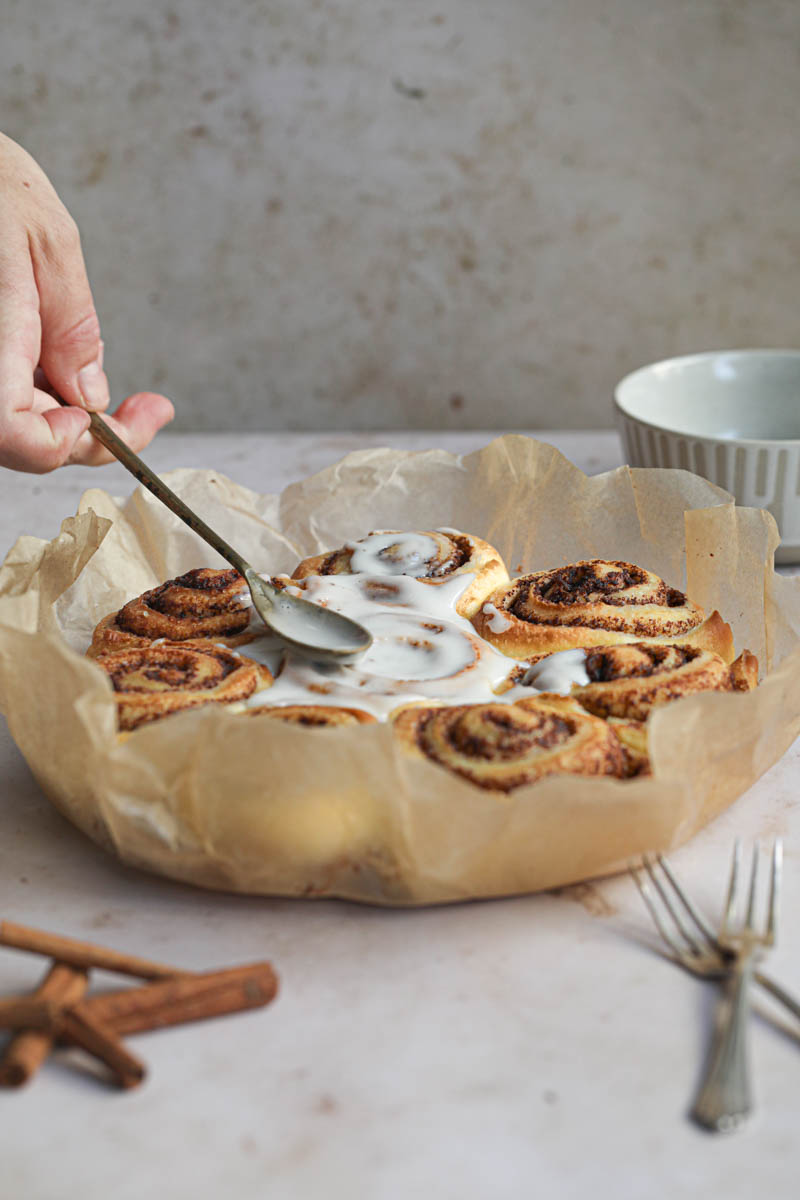 One hand spreading the glaze over the brioche cinnamon rolls.