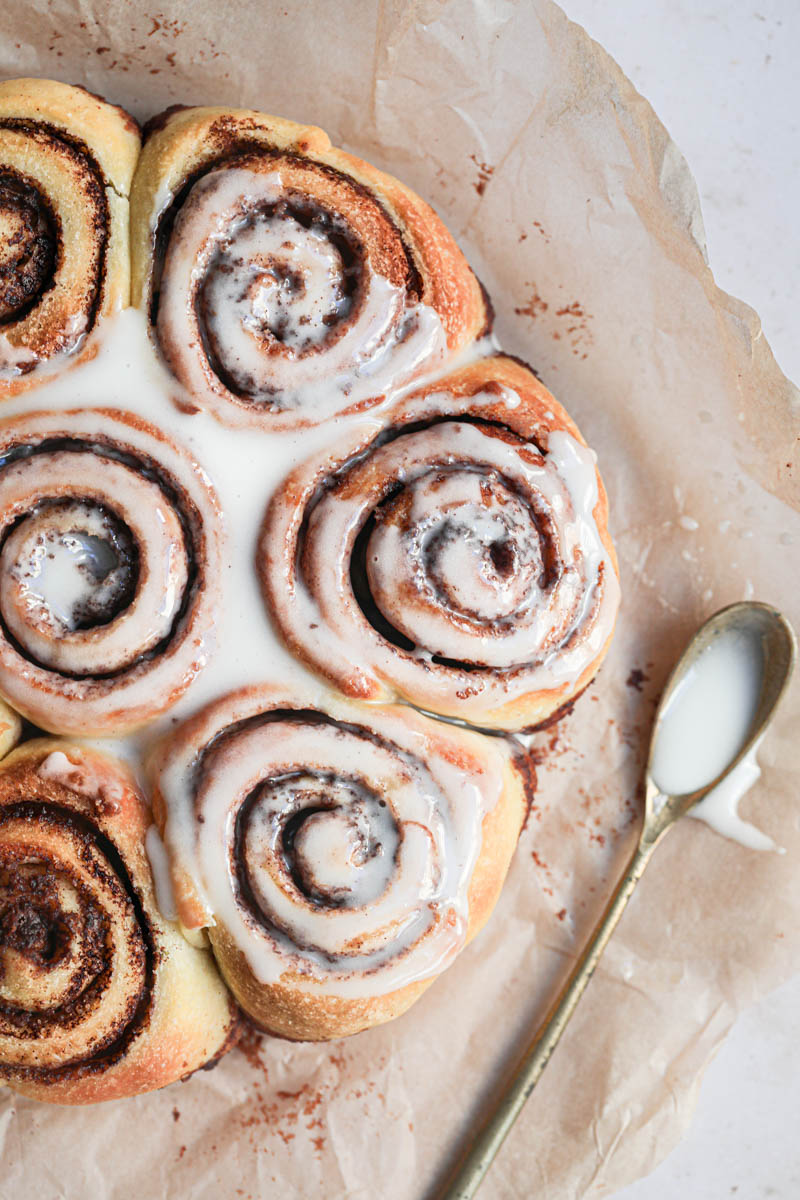 Closeup of the baked small batch cinnamon rolls on a piece of parchment paper with a spoon on the side.