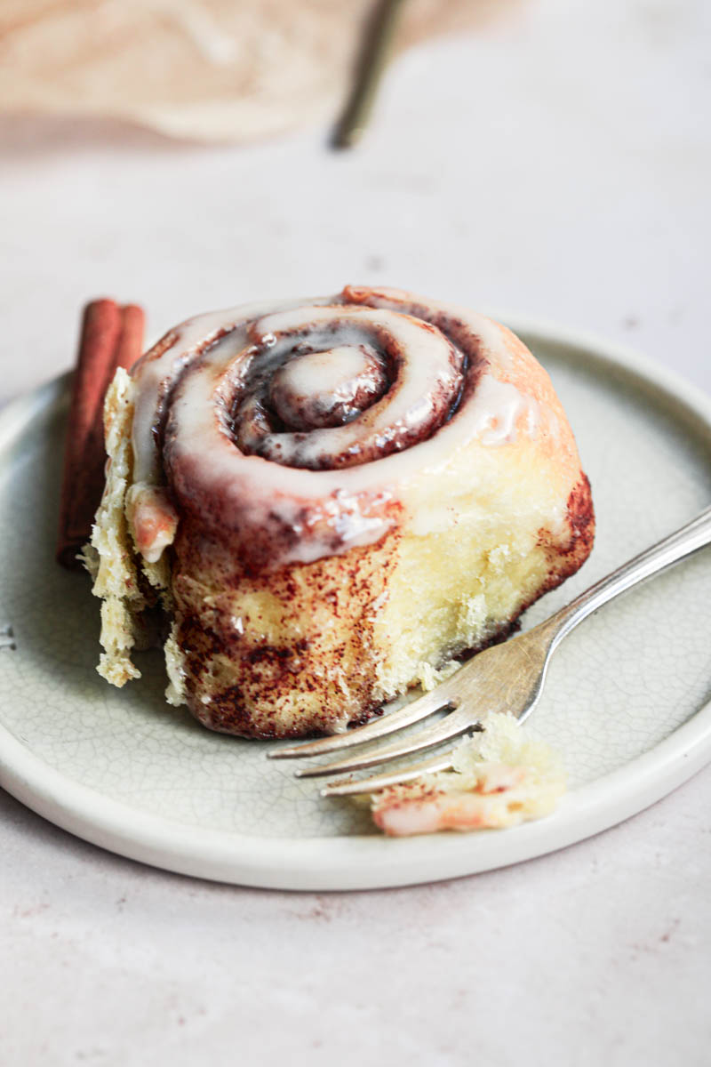 One cinnamon roll on a green plate with a small fork on the side.