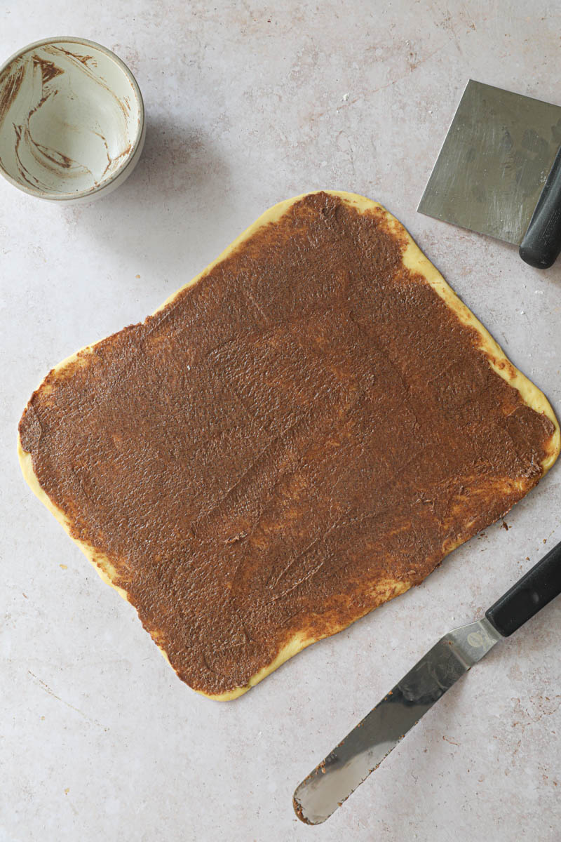 The brioche dough covered with the cinnamon filling with a small spatula on the side.