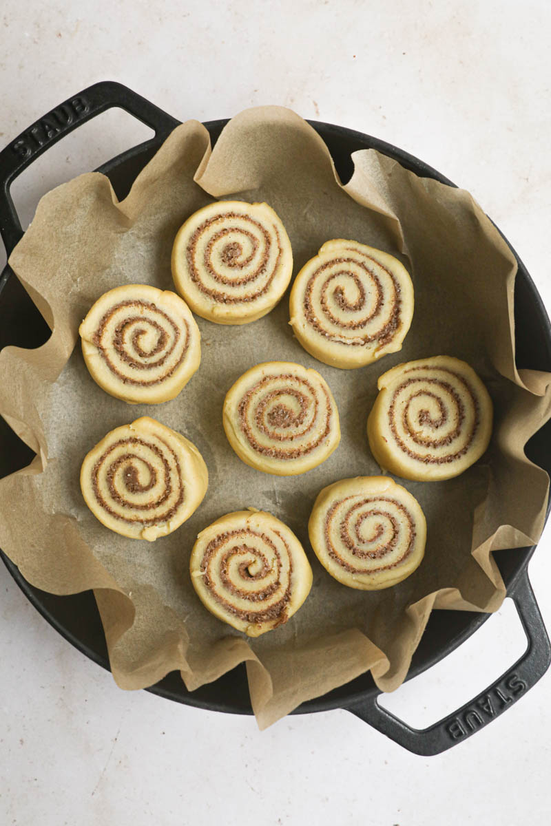 The cinnamon rolls, cut into small rolls placed inside a cast iron pan lined with parchment paper.