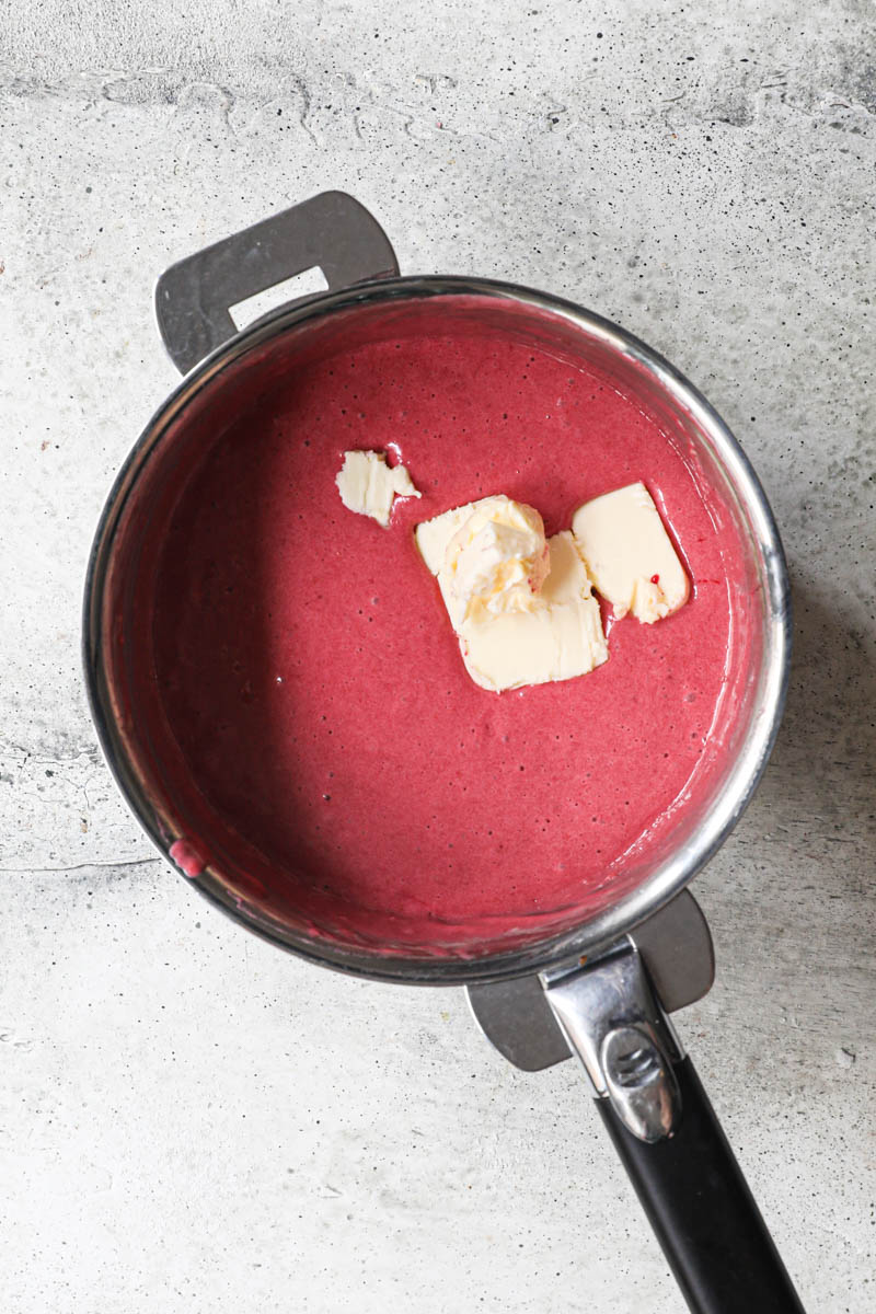 The cranberry curd with some pieces of butter on top inside a pan.