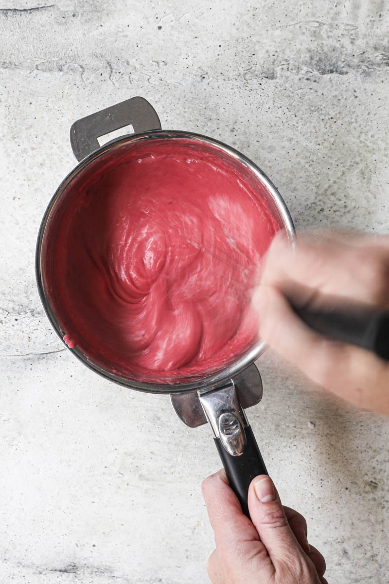 One hand whisking the butter into the cranberry curd.