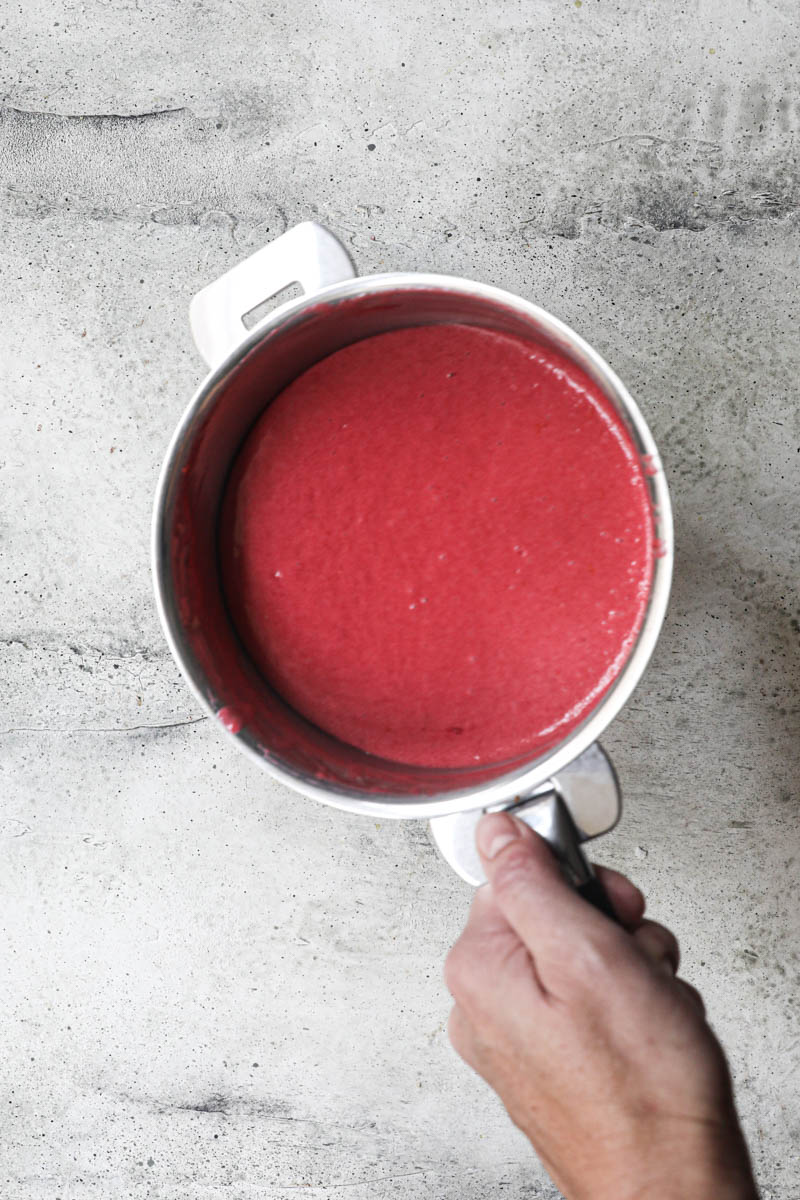 The finished cranberry curd inside a pan held by one hand.