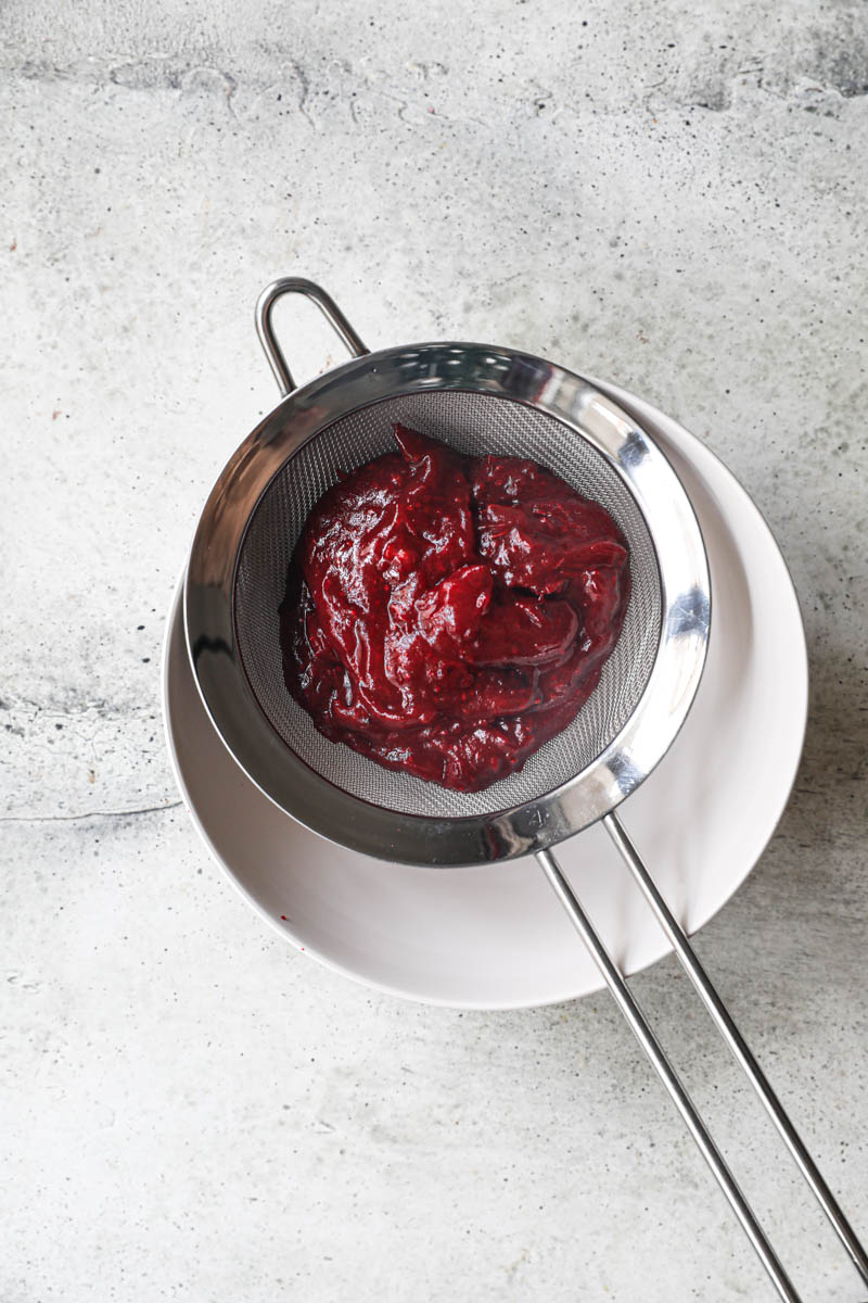The pureed cranberries inside a fine mesh sieve placed on top of a white bowl.