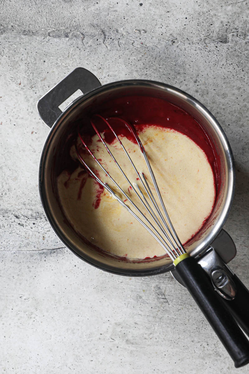The cranberry puree and the cremated yoks/sugar inside a pan with a whisk inside.