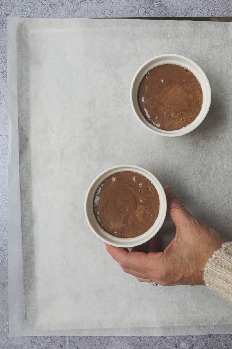 One hand holding the ramekin filled with the chocolate souffle batter ready to be baked.