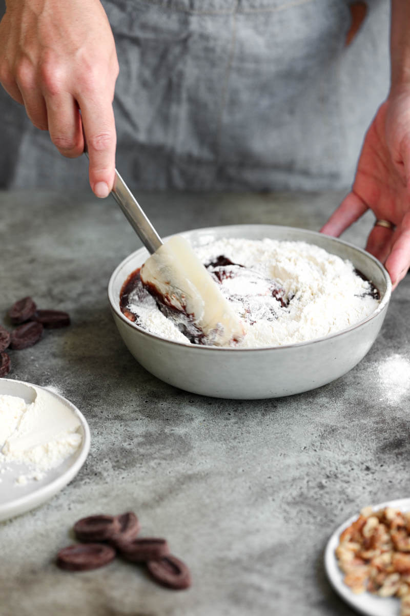 90° shot of 2 hands folding in the flour to the brownie batter