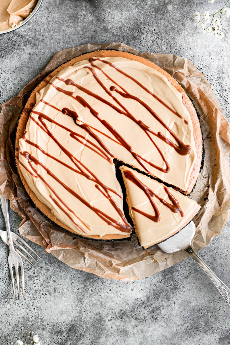The frosted dulce de leche cheesecake as seen from above with some forks on the side with a spatula slightly removing one slice of cake.