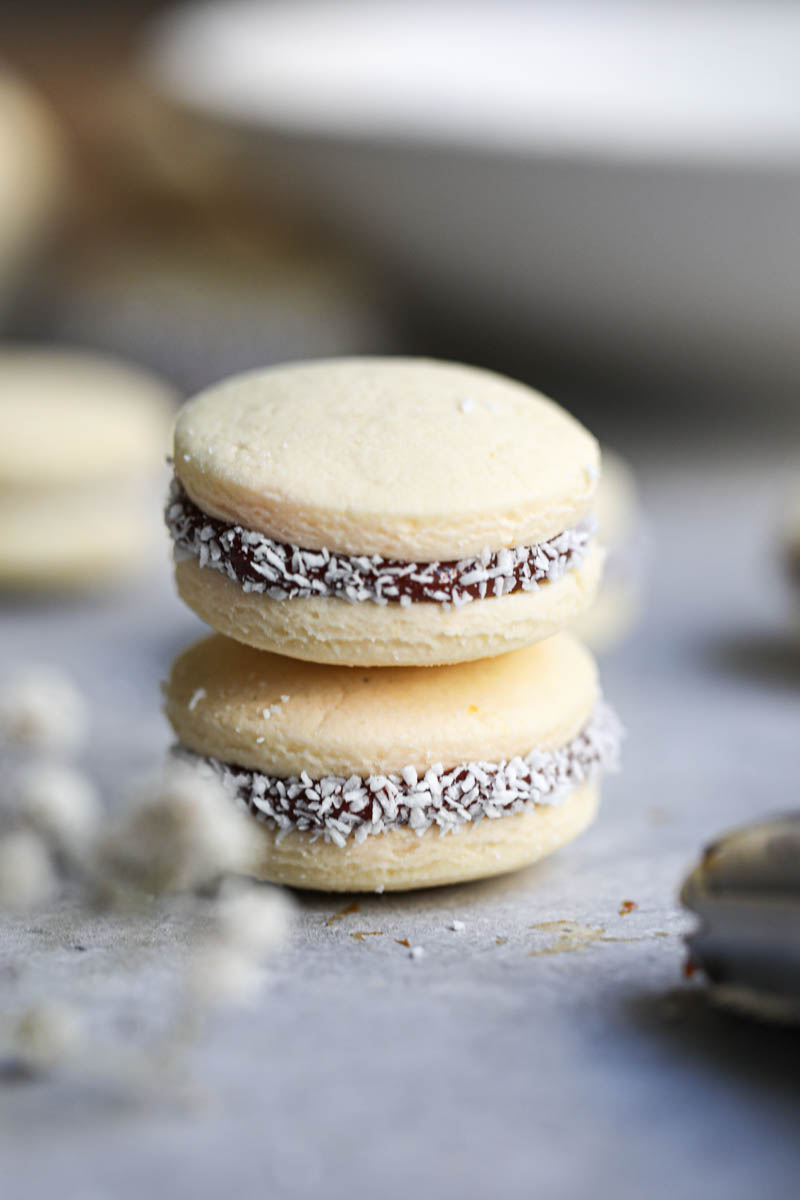 A stack of 2 corn-starch alfajores cookies with some flowers on the front of the frame.