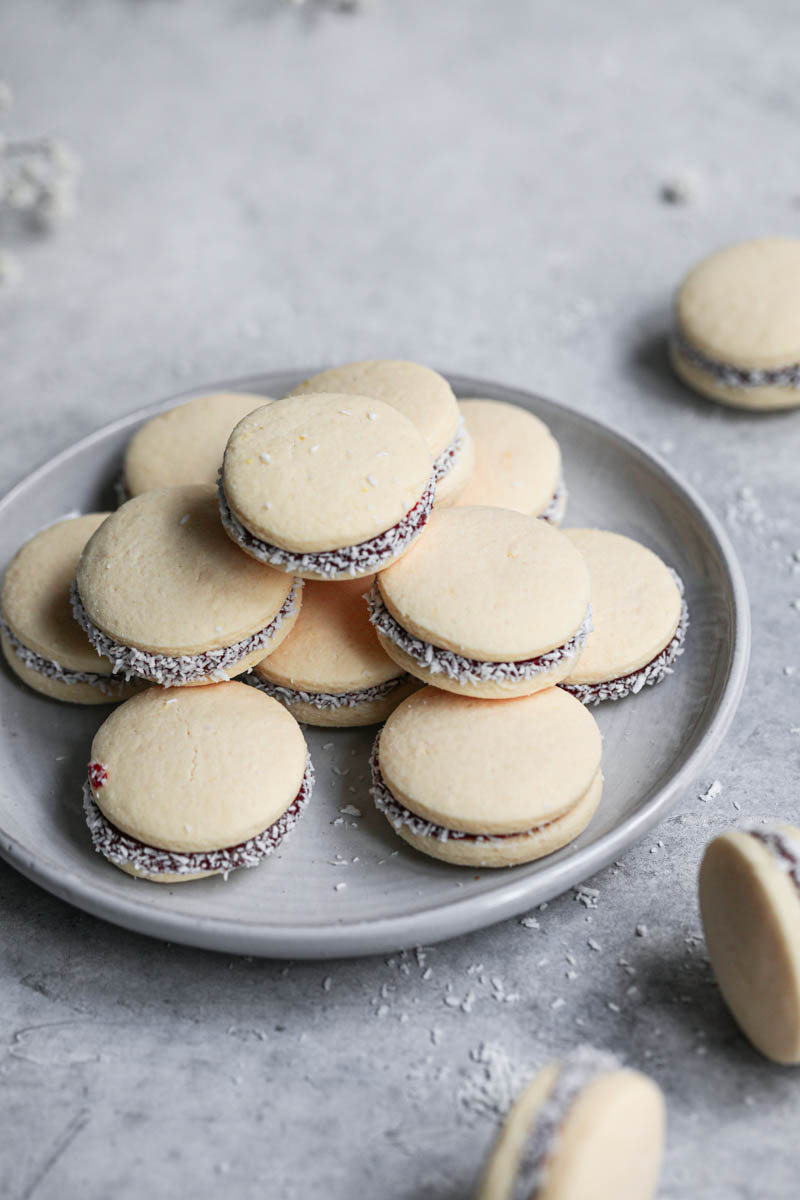 Alfajores stacked on top of a grey plate, and some alfajores on the right side of the frame.