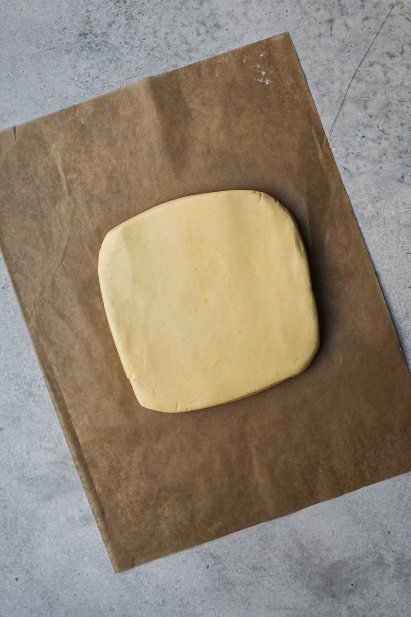 The alfajores cookies dough shaped as a rectangle on top of a piece of brown parchment paper.