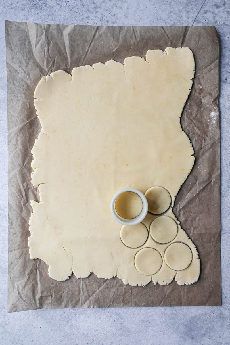 The rolled out cornstarch cookie dough on top of a parchment paper with a cookie cutter on top, and some cookies cut out.