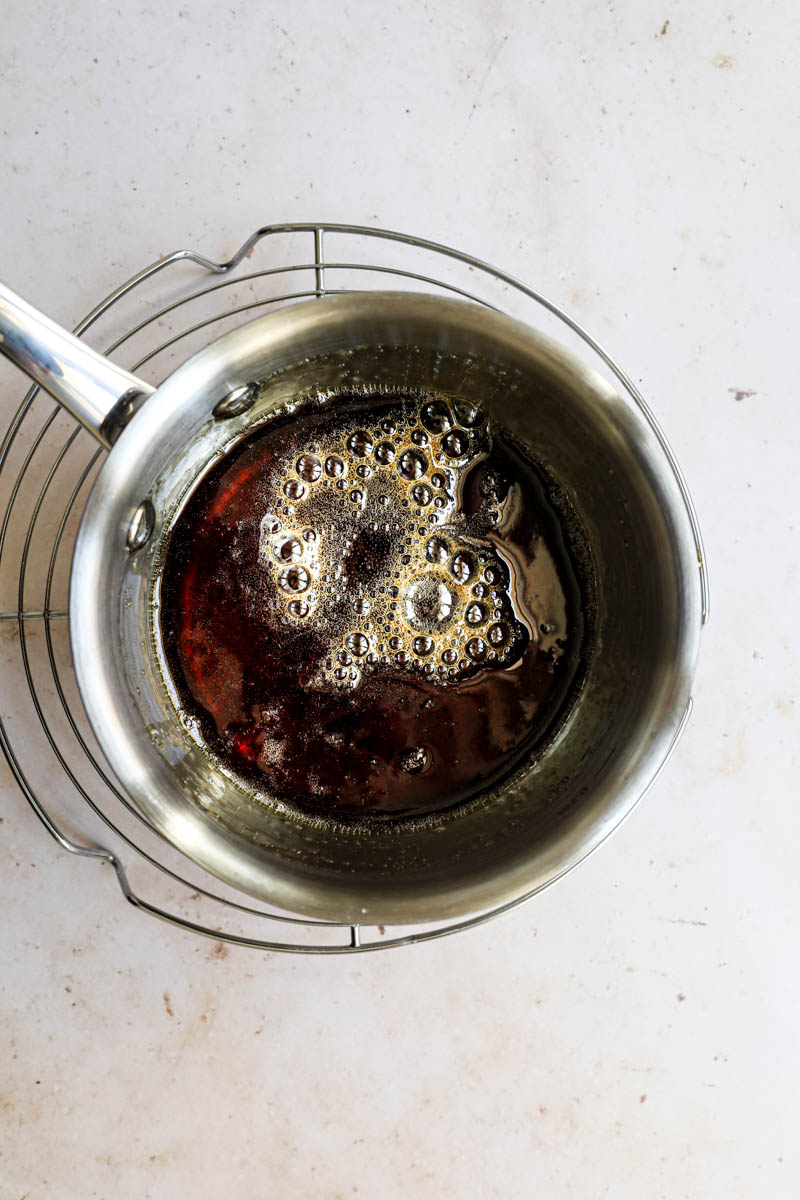 A pot with the cooked caramel for the dulce de leche flan placed on top of a wire rack.