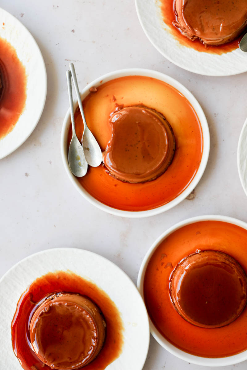 The mini-individual dulce de leche flan on white plates arranged in an irregular manner, as seen from above.